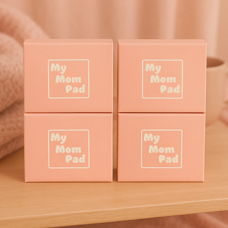Quatre boîtes roses "My Mom Pad" empilées, présentées sur une table en bois. Solution hygiénique post-partum en lot.