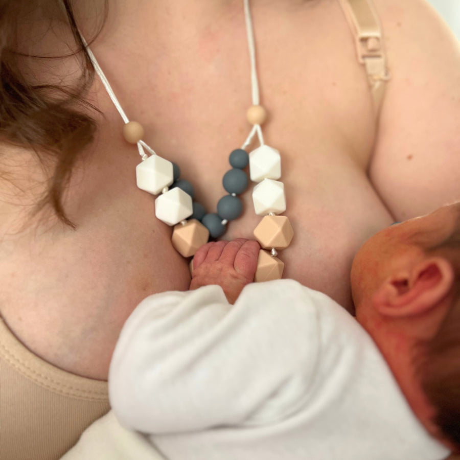Maman en brassière d’allaitement beige nourrissant son bébé en position madone utilisant un collier d'allaitement, le bébé tient le collier d'allaitement