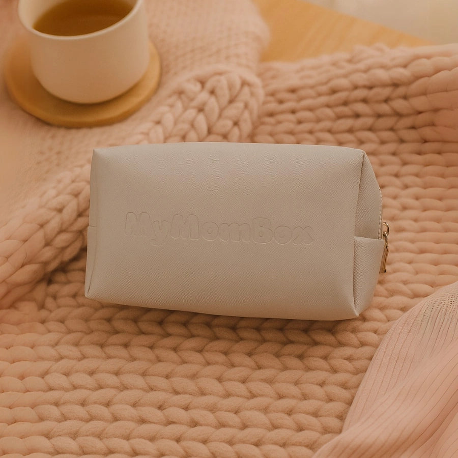 Trousse de toilette grise MyMomBox, élégante et pratique, posée sur une couverture tricotée rose. Idéale pour rassembler les essentiels post-partum.